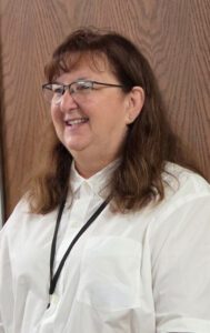 lady with long brown hair and white shirt on wood grain background -Department Convention can'trun without the help of great host unit volunteers, such as Unit 2 Treasurer Amelia Tintes.